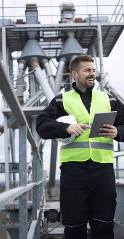 Industrial factory worker standing on high metal construction of production plant.